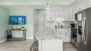 A modern kitchen with a marble countertop, stainless steel appliances, and a flat-screen TV mounted on the wall. - Beachside Abode 1A (Old Orchard Beach)