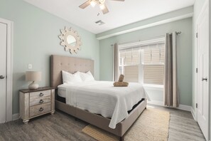 A bedroom with a bed, nightstand, lamp, decorative mirror, and a window with curtains.