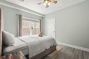 Ein Schlafzimmer mit einem Bett, einem Deckenventilator, einem Fenster mit Vorhängen und einer Tür.