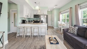 A spacious kitchen with a central island, white cabinetry, and a dining area with a table and chairs. - Beachside Abode 2A (Old Orchard Beach)