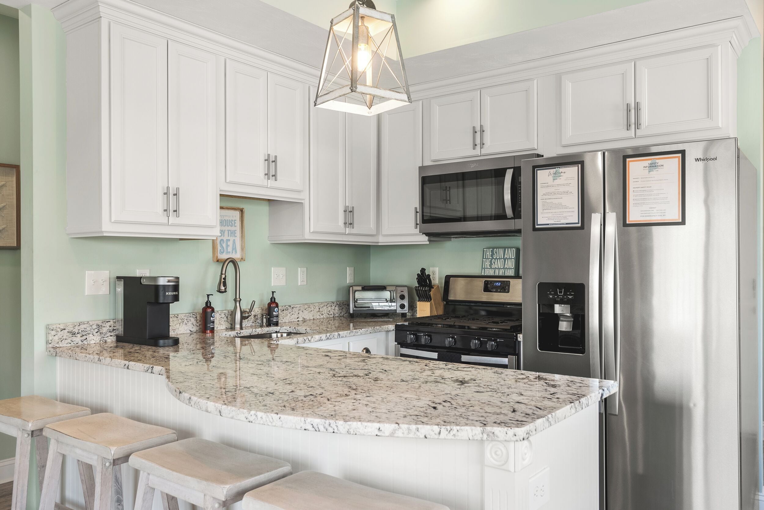 A kitchen with white cabinets, a stainless steel refrigerator, a microwave, a stove, and a coffee maker.