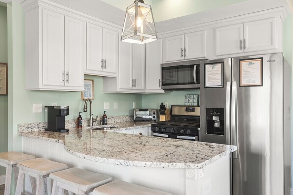 A kitchen with white cabinets, a stainless steel refrigerator, a microwave, a stove, and a coffee maker.
