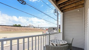 A balcony with wicker furniture, a view of a road, and a building with a sign. - Beachside Abode 2A (Old Orchard Beach)