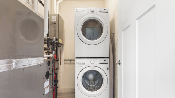 A laundry room with two stacked front-loading washing machines, a water heater, and a door. - Beachside Abode 2A (Old Orchard Beach)