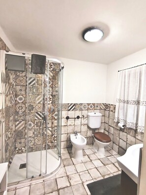 A bathroom with a shower enclosure, a toilet, a bidet, and a sink.