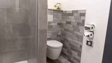 Ein Badezimmer mit Toilette, Dusche und einem an der Wand befestigten Toilettenpapierhalter.