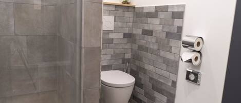 A bathroom with a toilet, a shower, and a wall-mounted toilet paper dispenser.