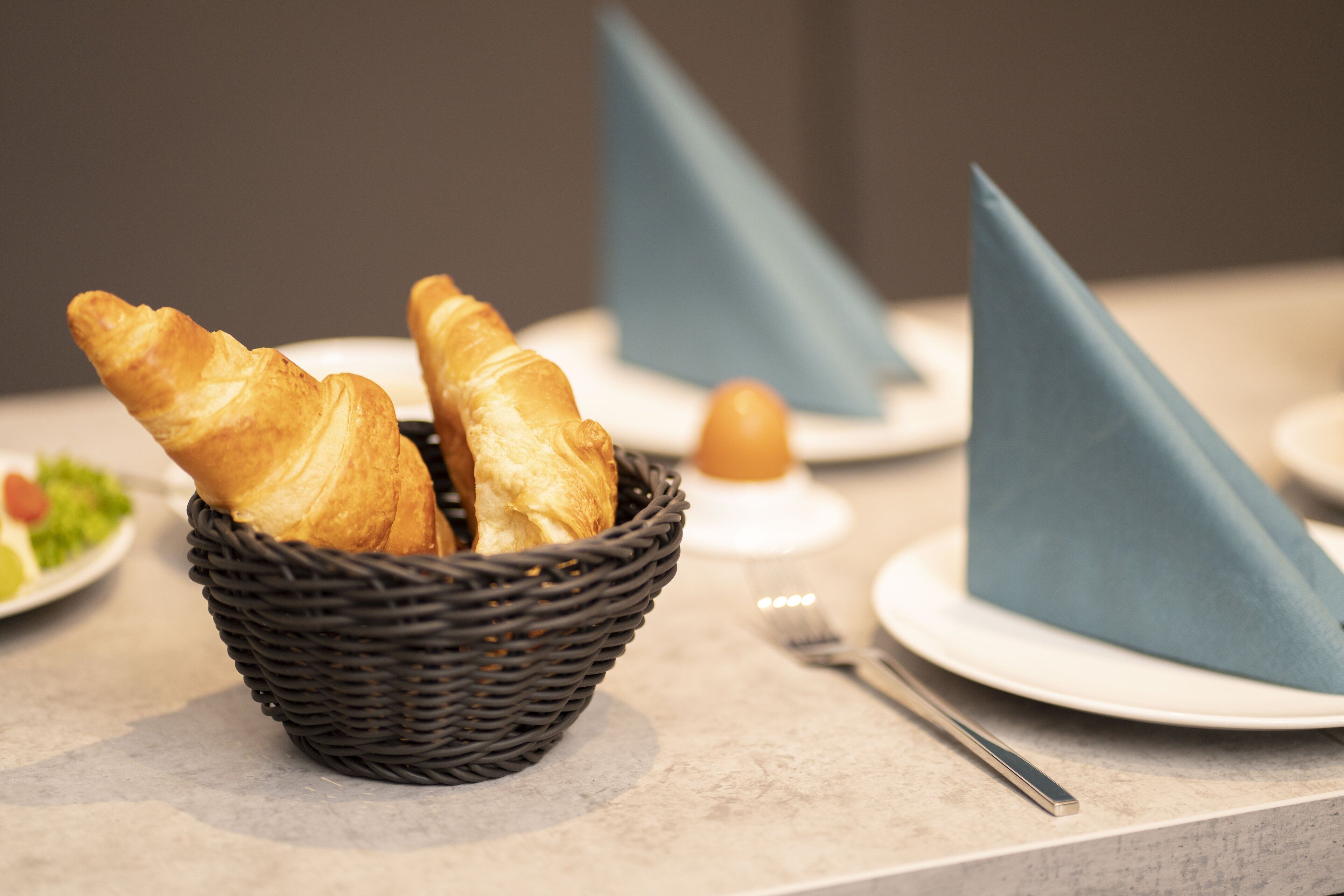 Una cesta de cruasanes sobre una mesa, con un tenedor y una servilleta.