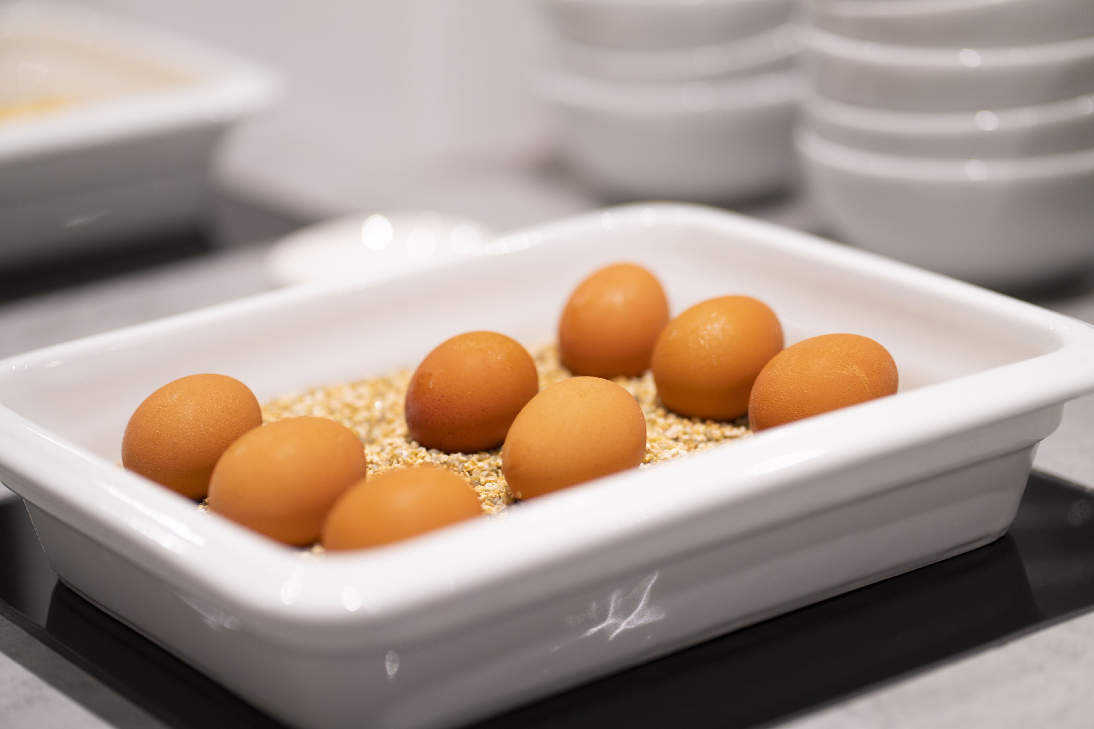 A white rectangular dish containing several brown eggs and some grains.
