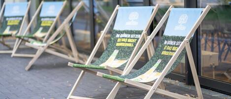 Sillas de madera al aire libre con información impresa en los respaldos, dispuestas sobre una superficie pavimentada.