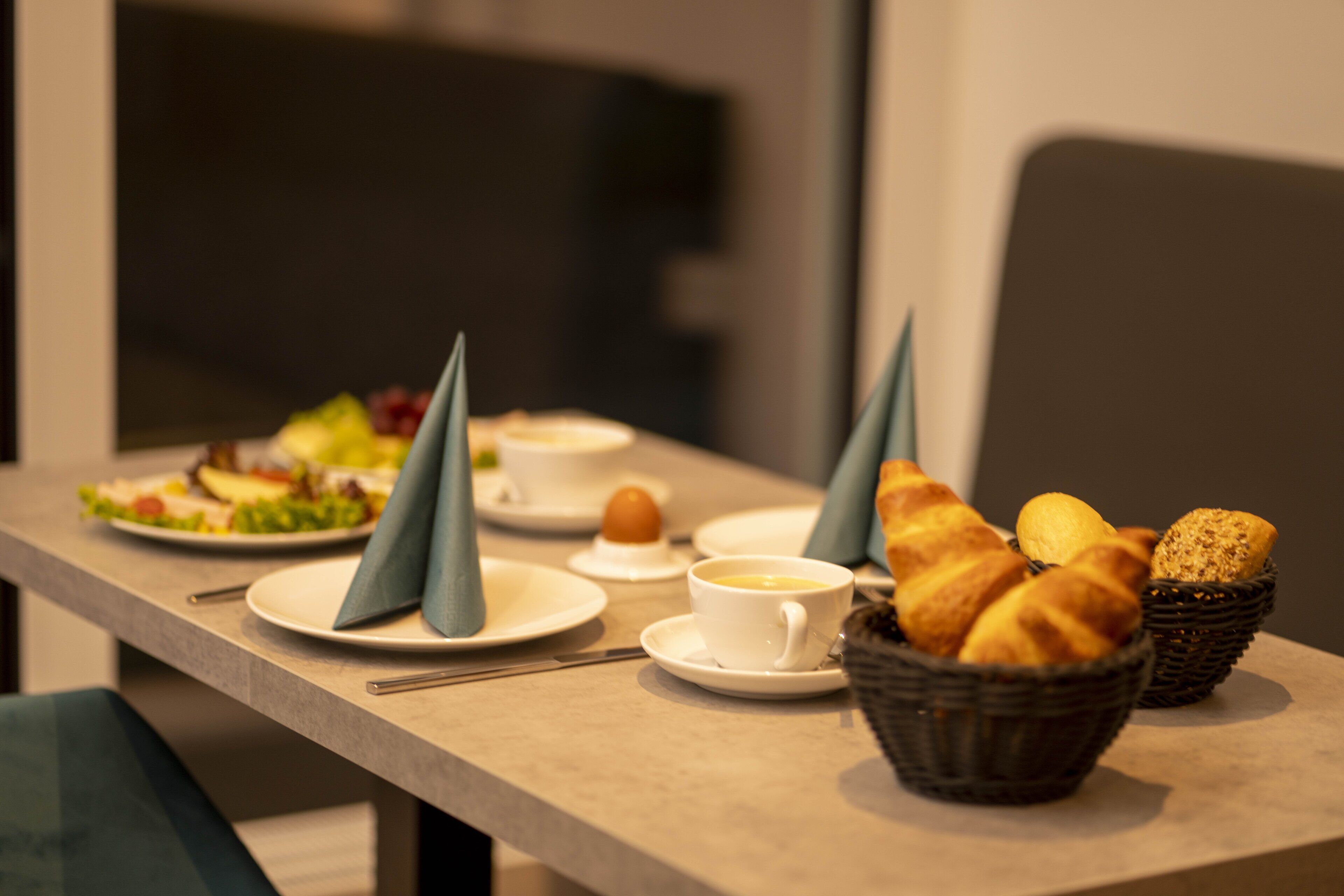 A breakfast setting with croissants, bread, and a cup of coffee on a table.