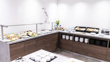 A buffet setup with various food items, including salads, fruits, and pastries, arranged on a counter with a modern design.