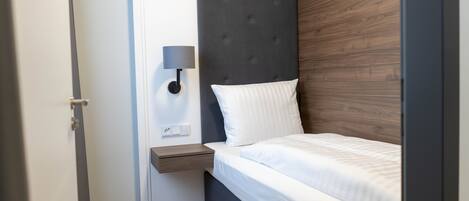A bedroom with a bed, a nightstand, a wall-mounted lamp, and a wooden headboard.