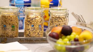 Drei Glaskolben mit Müsli und Metallverschlüssen, eine Schüssel mit gemischten Früchten und ein blau-gelb verpacktes Produkt im Hintergrund.