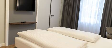 Habitación de hotel con cama, televisor montado en la pared, puerta y ventana con cortinas.