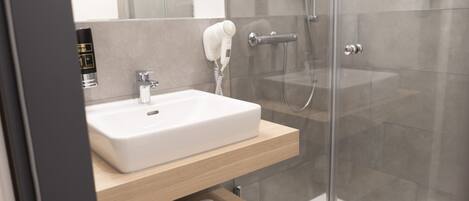 A modern bathroom with a white sink, a hairdryer, and a glass-enclosed shower.