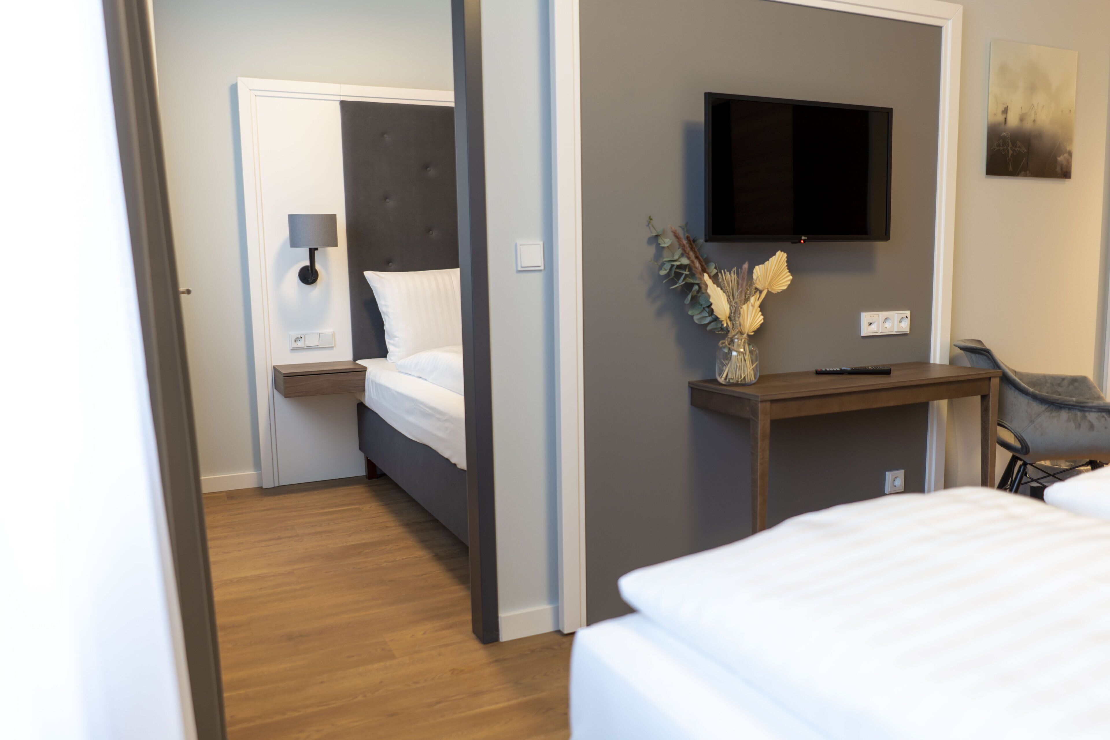 A hotel room with a bed, bedside table, lamp, and a mounted TV.