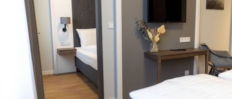 Una habitación de hotel con cama, mesita de noche, lámpara y televisor montado.