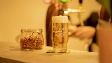 Een glas Carlsberg bier op een onderzetter, met een potje noten op de achtergrond.