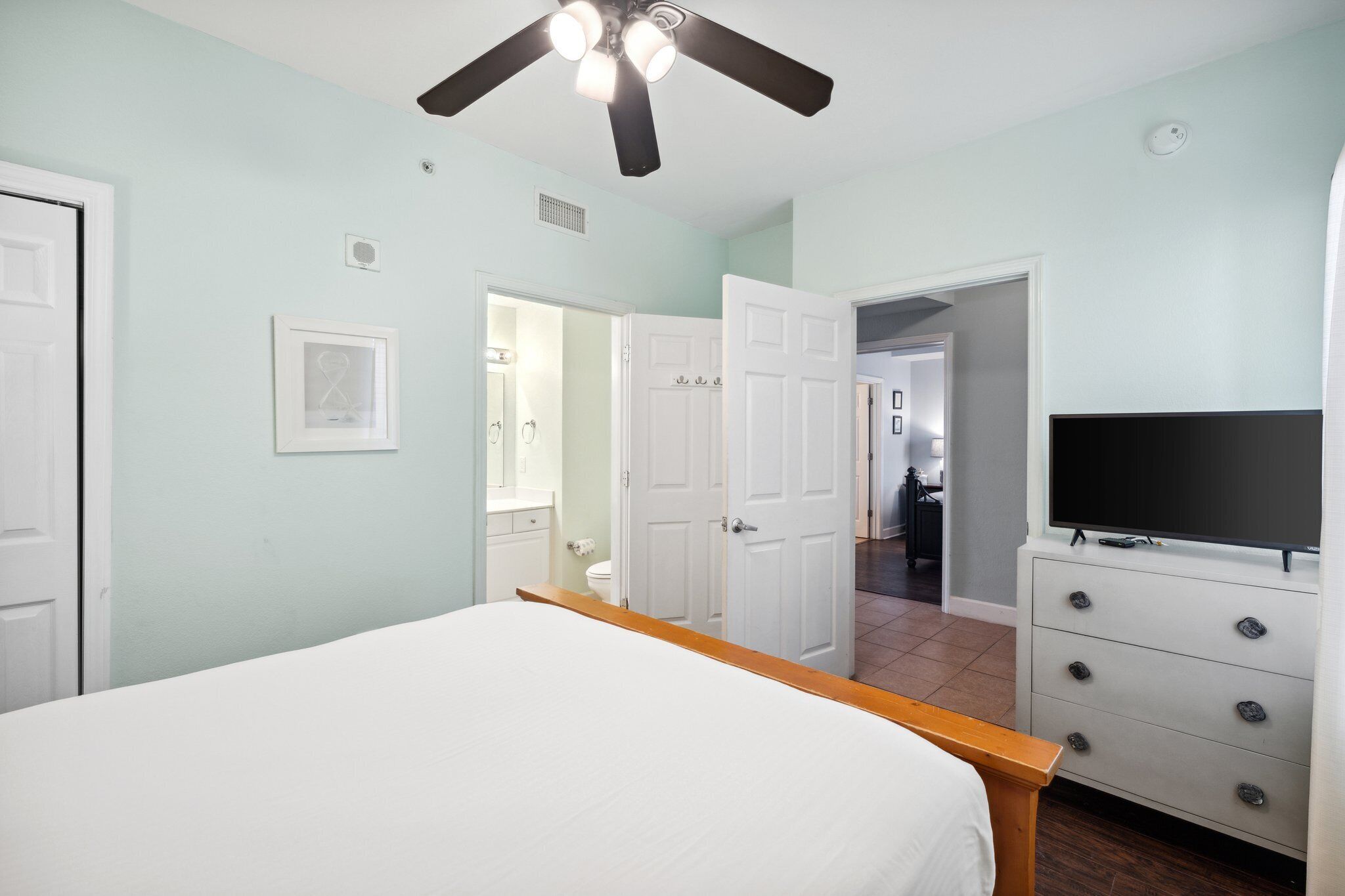 A bedroom with a bed, a TV, a dresser, and a ceiling fan.