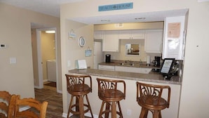 A kitchen with a bar area, wooden chairs, and a sign that reads 'BEACH HOUSE'.