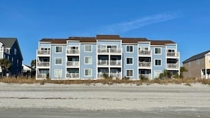 A multi-story residential building with balconies, located near a sandy beach.