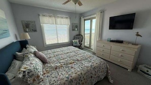 A bedroom with a bed, a dresser, a ceiling fan, a TV, and a window with curtains.