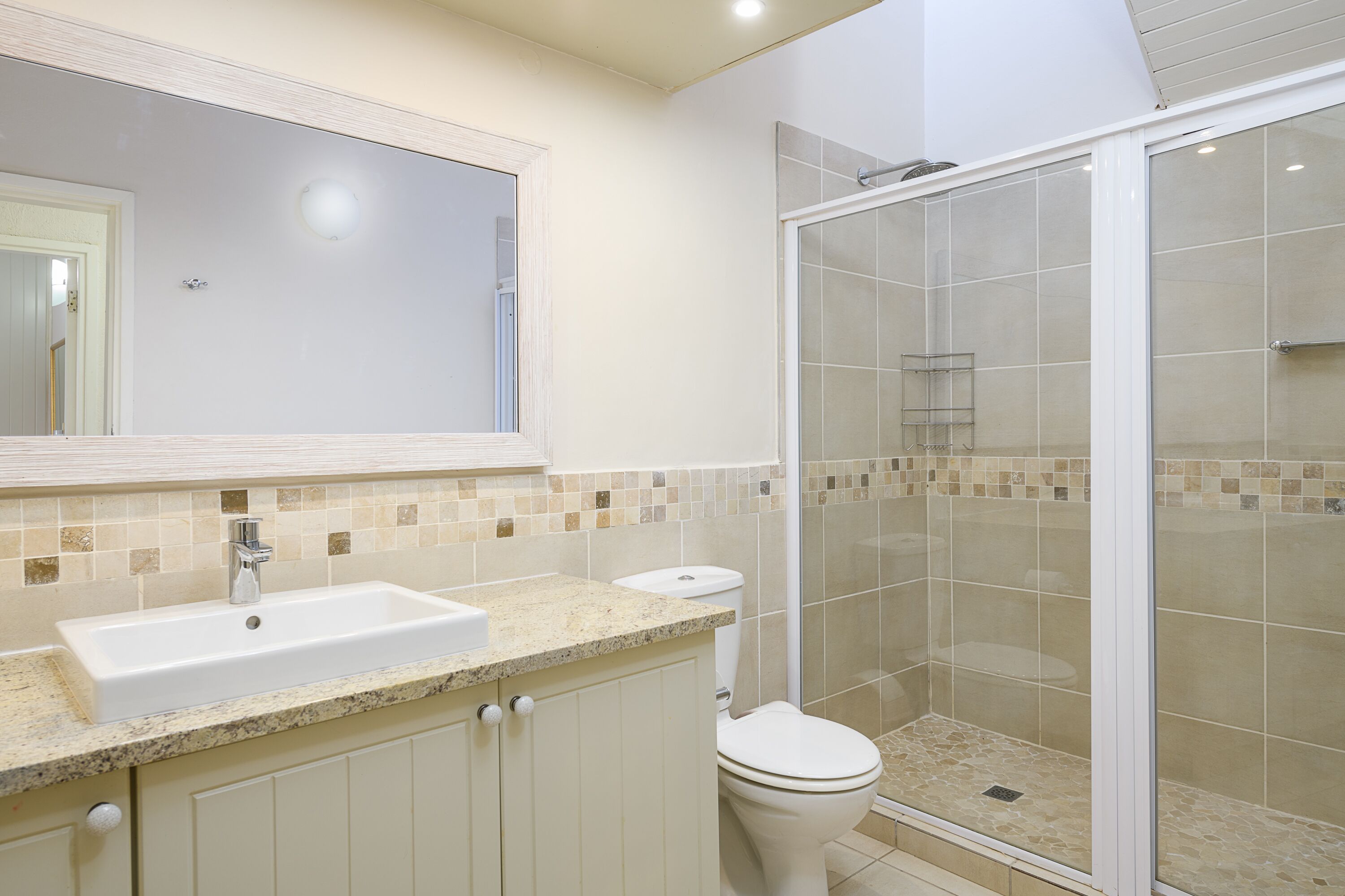Un baño con lavamanos, inodoro y ducha con mampara de vidrio.