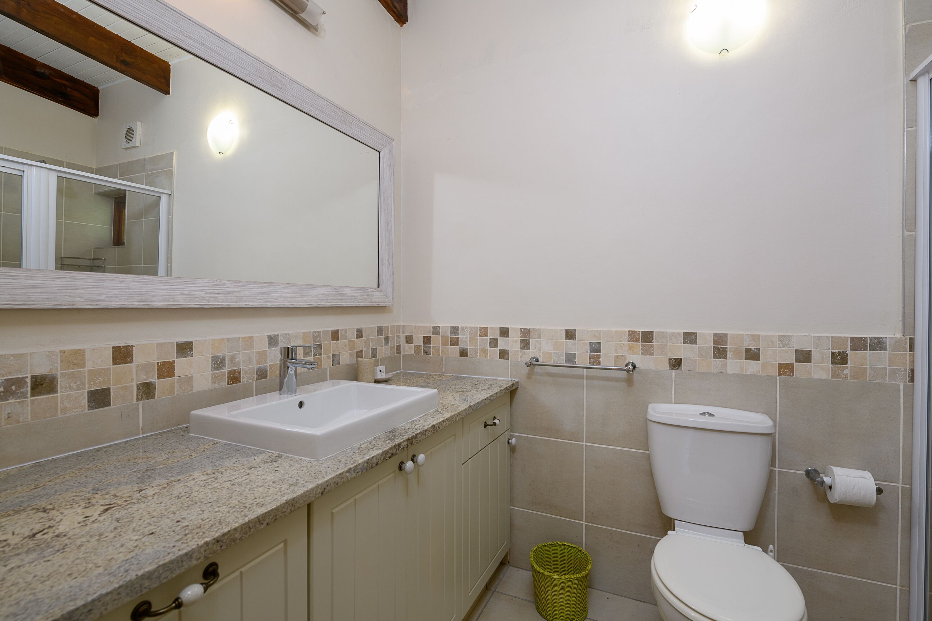 A bathroom with a sink, mirror, toilet, and a trash bin.