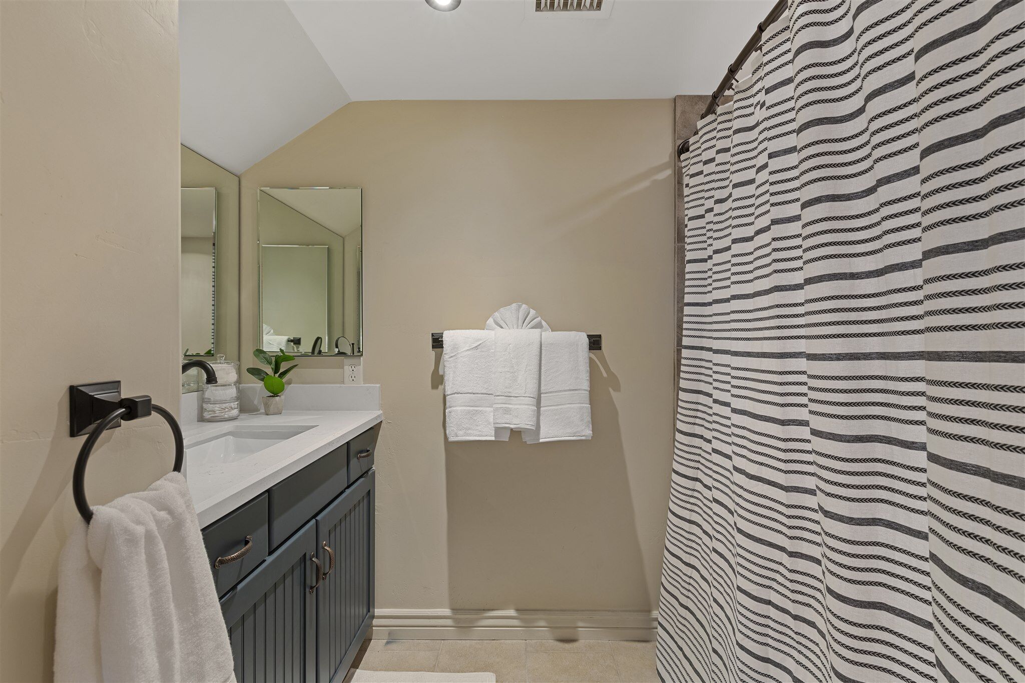 A modern bathroom with a large mirror, a sink with a towel ring, and a striped shower curtain.