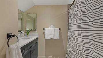 A modern bathroom with a large mirror, a sink with a towel ring, and a striped shower curtain.