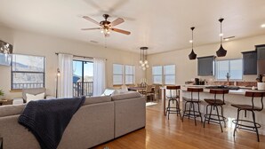 A spacious living area with a sofa, a ceiling fan, and a kitchen area with bar stools and pendant lights. - Large Private Home in Jerome, AZ w/ Full Kitchen (Jerome)