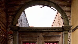 An arched doorway with wooden panels and red curtains, leading to a courtyard with debris and a brick wall. - Large Private Home in Jerome, AZ w/ Full Kitchen (Jerome)