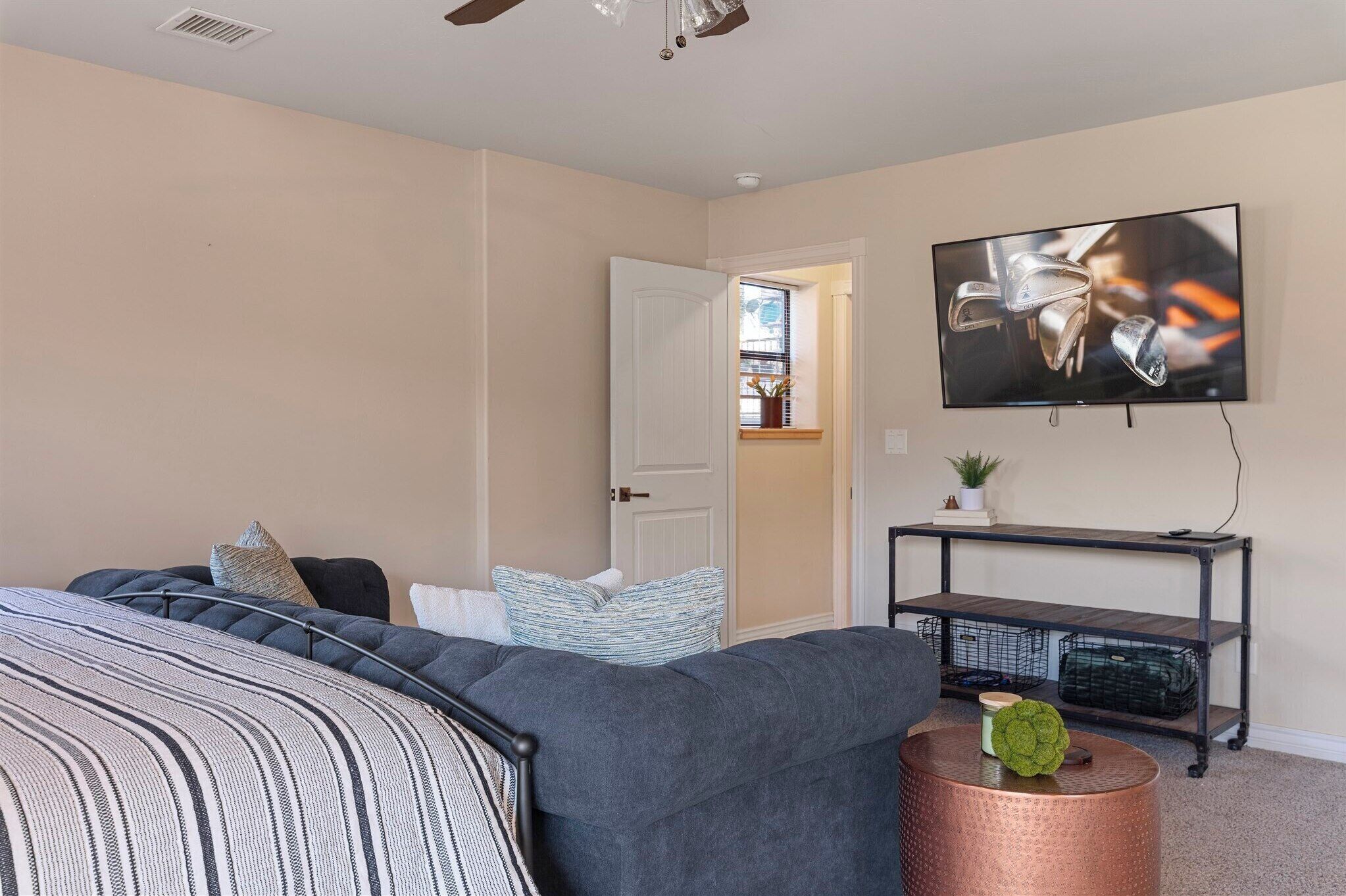A bedroom with a bed, a television mounted on the wall, a small table, and a door leading to another room.