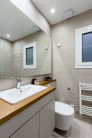 Ein modernes Badezimmer mit einem großen Spiegel, einem weißen Waschbecken, einer Toilette und einem Handtuchhalter.