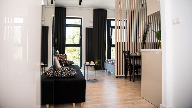 Una sala moderna con un sofá negro, una mesa de comedor de madera y un separador a rayas.