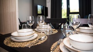 Una mesa de comedor dispuesta con platos blancos, copas con detalles dorados y cubiertos, con un mantel tejido.