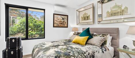 Une chambre avec un grand lit, une fenêtre donnant sur la forêt et plusieurs tableaux encadrés accrochés au mur.