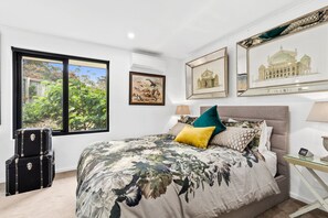 A bedroom with a large bed, a window with a view of trees, and several framed pictures on the wall.