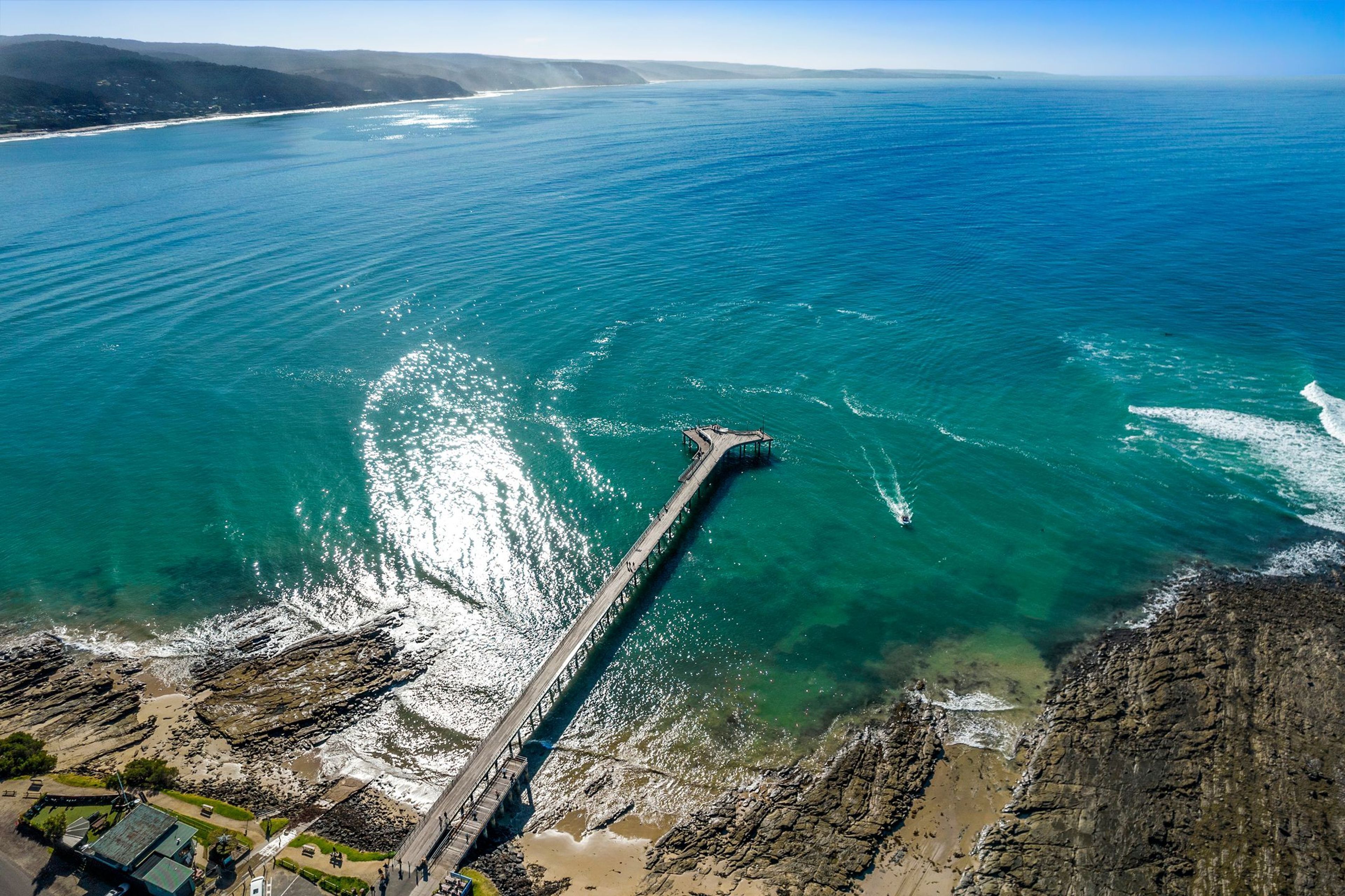 A coastal landscape with a long pier extending into the sea, rocky cliffs, and a clear sky.