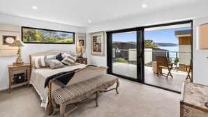 Ein Schlafzimmer mit Bett, einer Bank und einer großen Schiebetür zu einem Außenbereich mit Meerblick.