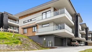 Ein modernes Mehrfamilienhaus mit Balkonen, einer Garage und einer abschüssigen Auffahrt.