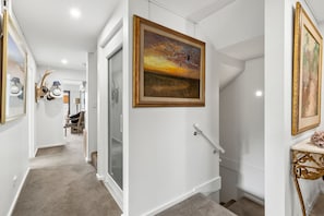 Un pasillo con una escalera, un cuadro y una lámpara decorativa en la pared.