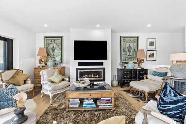 A modern living room with a fireplace, comfortable seating, a coffee table with books, and decorative items.