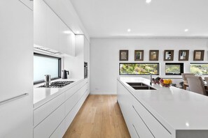 A modern kitchen with white cabinetry, a central island, and a view of greenery outside.