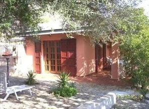 A small, single-story building with a red exterior and a wooden door. There is a small garden area with a bench and a lamp post.