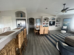 A spacious living area with a dining table, wicker chairs, a sofa, and a television.