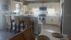 A kitchen with white cabinets, a central island with bar stools, a microwave, stove, and a sink. - Winds of Change - Easy Beach Access (Bolivar Peninsula)