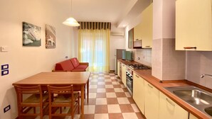 A compact kitchen with a dining area, a sofa, and a TV. - Appartamento Adriana 2 - Carraro Immobiliare Jesolo (Lido di Jesolo)