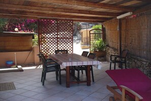 Um pátio externo com mesa e cadeiras de madeira, uma poltrona vermelha e uma parede de pedra.